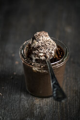 Glass and spoon of chocolate pudding with vanilla sauce on wooden table, close up - SBD000037