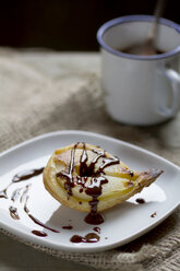 Pear in puff pastry on plate with mug of chocolate sauce, close up - SBD000058