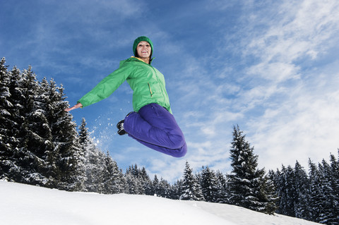 Österreich, Salzburg, Porträt einer jungen Frau, die in den Schnee springt, lächelnd, lizenzfreies Stockfoto
