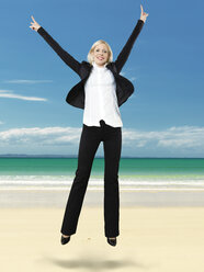 Porträt einer Geschäftsfrau, die lächelnd an den Strand springt - STKF000265