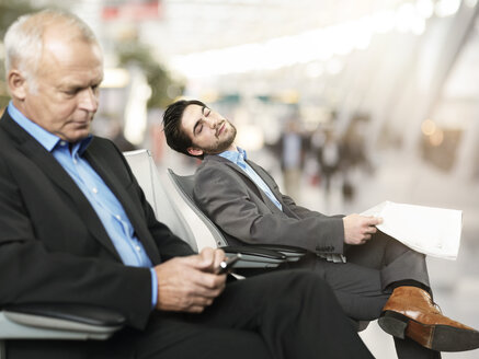 Senior man using mobile phone while mid adult man sleeping in background - STKF000263