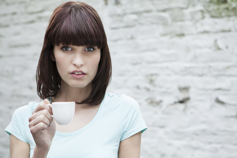 Deutschland, Köln, Porträt einer jungen Frau mit Kaffeetasse, lizenzfreies Stockfoto