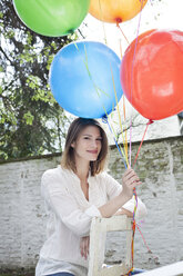 Deutschland, Köln, Junge Frau hält Luftballons, lächelnd - FMKF000801