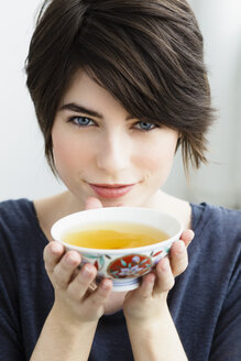 Deutschland, Bayern, München, Porträt einer jungen Frau mit Teetasse, lächelnd - SPOF000386