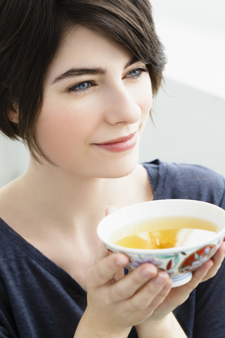 Deutschland, Bayern, München, Junge Frau hält Teetasse, lächelnd, lizenzfreies Stockfoto