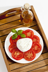 Büffelmozzarella mit Basilikum, Tomaten und einer Flasche Olivenöl auf einem Teller, Nahaufnahme - CSF019168
