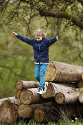 Germany, Baden Wuerttemberg, Girl jumping from wooden logs - SLF000121