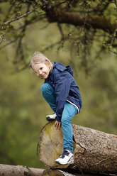 Germany, Baden Wuerttemberg, Portrait of girl climbing on wooden logs, smiling - SLF000140