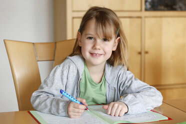 Germany, Baden Wuerttemberg, Portrait of girl doing her homework, smiling - SLF000094