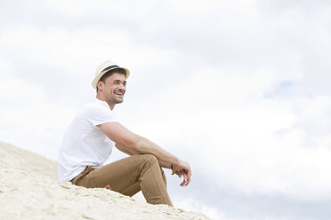Deutschland, Bayern, Junger Mann sitzt auf Sand, lächelnd - MAEF006759