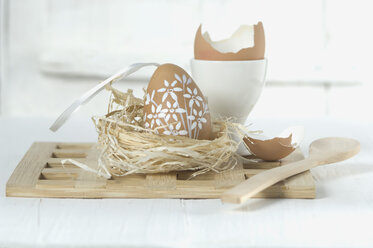Painted easter egg in straw nest with wooden spoon on white background - ASF004972