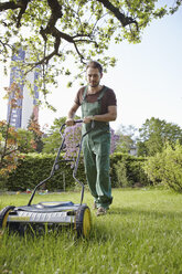 Deutschland, Köln, Junger Mann beim Rasenmähen mit Schubmäher - RHYF000433