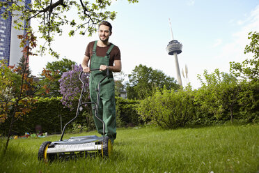 Deutschland, Köln, Junger Mann beim Rasenmähen mit Schubmäher - RHYF000432