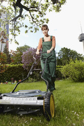 Germany, Cologne, Young woman mowing lawn with push mower - RHYF000431