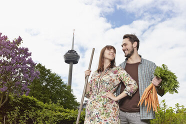 Deutschland, Köln, Junges Paar mit Karottenstrauß, lächelnd - RHYF000438