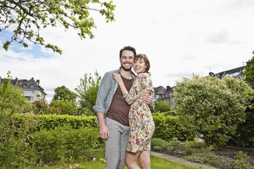 Deutschland, Köln, Junges Paar umarmt sich im Garten, lächelnd - RHYF000415