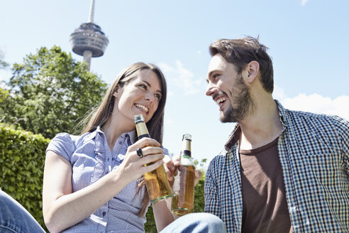 Deutschland, Köln, Junges Paar hält Bierflaschen, lächelnd - RHYF000410