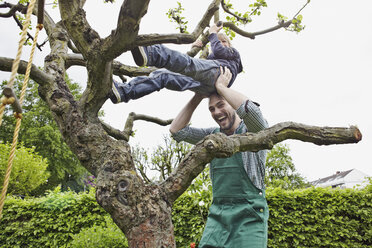 Deutschland, Köln, Vater hilft Sohn beim Klettern auf Baum, lächelnd - RHYF000388