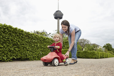 Deutschland, Köln, Mutter trägt Tochter in Spielzeugauto, lächelnd - RHYF000378