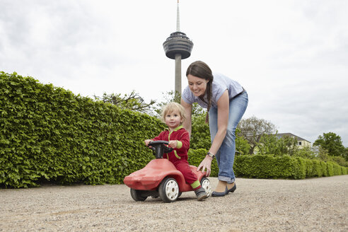 Deutschland, Köln, Mutter trägt Tochter in Spielzeugauto, lächelnd - RHYF000378