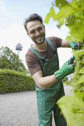 Germany, Cologne, Portrait of young man cutting leaves, smiling - RHYF000457
