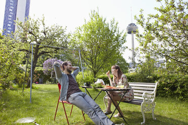 Germany, Cologne, Young couple having breakfast in garden, smiling - RHYF000454