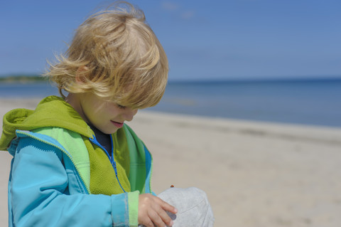 Deutschland, Mecklenburg Vorpommern, Junge schaut auf Mütze am Strand, lizenzfreies Stockfoto