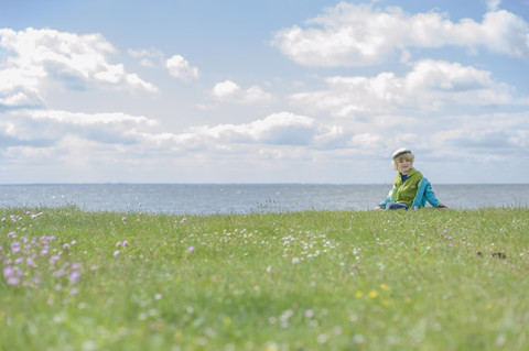 Deutschland, Mecklenburg Vorpommern, Junge sitzt im Gras an der Ostsee, lizenzfreies Stockfoto
