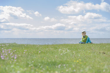 Deutschland, Mecklenburg Vorpommern, Junge sitzt im Gras an der Ostsee - MJF000179