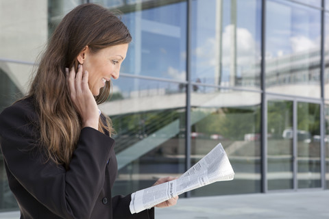 Germany, Berlin, Businesswoman reading newspaper, smiling stock photo