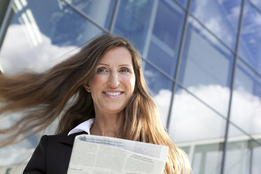 Germany, Berlin, Businesswoman holding newspaper, smiling - FKIF000004