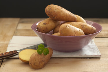 Bowl of potatoes with knife on wooden table, close up - OD000032