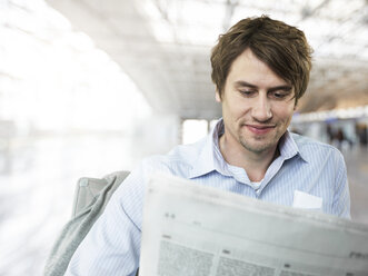 Geschäftsmann liest lächelnd eine Zeitung am Flughafen - STKF000290