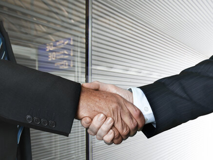 Businessmen shaking hands at airport, close up - STKF000281