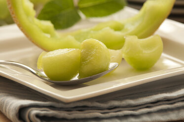 Plate of honeydew melon with spoon on napkin, close up - OD000034