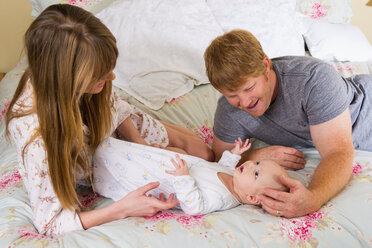 Eltern mit einem kleinen Jungen auf dem Bett, lächelnd - ABAF000896