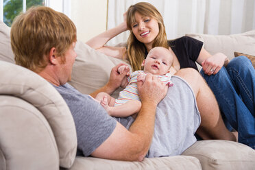 Eltern mit einem kleinen Jungen auf der Couch sitzend, lächelnd - ABAF000945