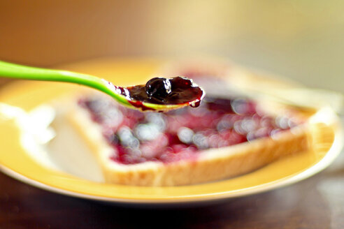 Germany, Spoon with black currant jam, toast with jam in background - SARF000044