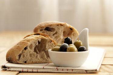 Spoon of olives with bread and napkin on wooden table, close up - OD000035