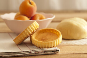 Bowl of apricots with dough and baking tartlets on wooden table, close up - OD000045