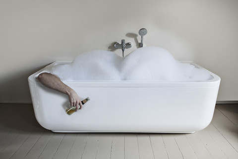 Mittlerer erwachsener Mann in der Badewanne mit Bierflasche, lizenzfreies Stockfoto