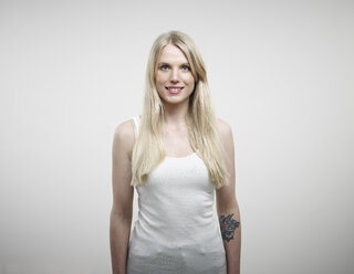 Portrait of young woman standing against white background, smiling - RH000250