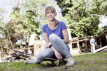 Germany, North Rhine Westphalia, Cologne, Mother sitting on skateboard while son standing in background - FMKYF000505