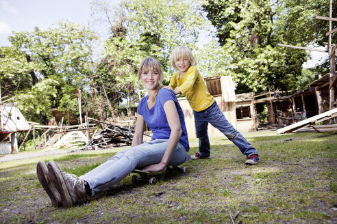 Germany, North Rhine Westphalia, Cologne, Mother and son playing with skateboard, smiling - FMKYF000433