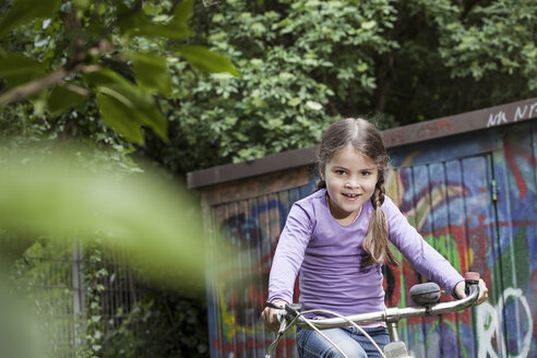 Germany, North Rhine Westphalia, Cologne, Girl riding bicycle in playground, smiling - FMKYF000448