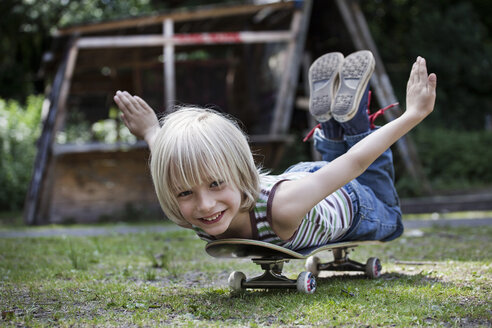 Deutschland, Nordrhein-Westfalen, Köln, Porträt eines auf einem Skateboard liegenden Jungen, lächelnd - FMKYF000451