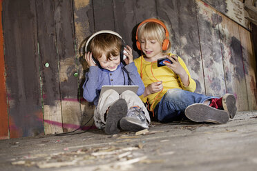 Deutschland, Nordrhein-Westfalen, Köln, Jungen hören Musik auf dem Spielplatz, lächelnd - FMKYF000428