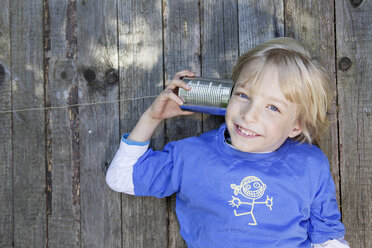 Germany, North Rhine Westphalia, Cologne, Portrait of boy listening to tin can phone, smiling - FMKYF000431