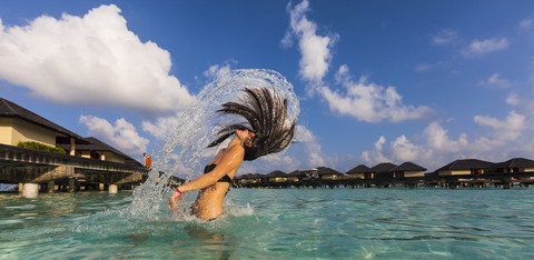 Malediven, Junge Frau spritzt mit nassen Haaren in der Lagune, lizenzfreies Stockfoto