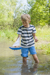 Germany, Bavaria, Munich, Boy playing with boat in lake - NH001400